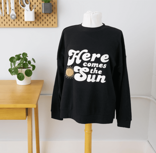 A black sweatshirt with the words " here comes the sun ".